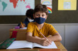 © Wavebreak Media - Portrait of a boy wearing face mask writing while sitting on his desk at school