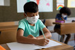 © Wavebreak Media - Boy wearing face mask writing while sitting on his desk at school
