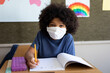 © Wavebreak Media - Portrait of boy wearing face mask writing while sitting on his desk at school