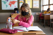 © Wavebreak Media - Girl wearing face mask sanitizing her hands while sitting on her desk at school