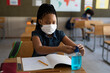 © Wavebreak Media - Black African American Girl wearing face mask sanitizing her hands while sitting on her desk at school