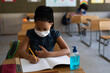© Wavebreak Media - Black African American Girl wearing face mask writing while sitting on her desk at school
