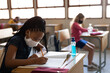 © Wavebreak Media - Black African American Girl wearing face mask writing while sitting on her desk at school