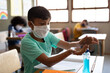 © Wavebreak Media - Boy wearing face mask sanitizing his hands while sitting on his desk at school