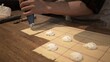 © diproduction - Stuffing ravioli on wooden table at the restaurant kitchen. Male hands squeezing filling from pastry bag to make tortellini, process of italian food making