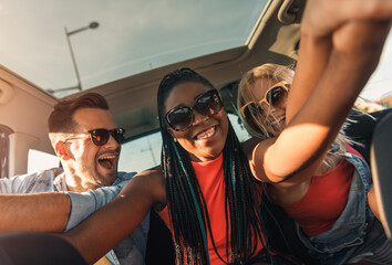 Wall Mural - Three best friends enjoying traveling in the car, sitting in rear seat and having lots of fun on a road trip.