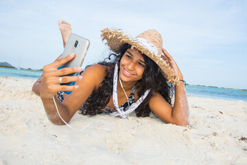 Wall Mural - Hispanic woman sun tanned enjoying lying down using social media with mobile on sand caribbean beach