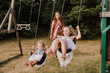 © Sara Monika/Westend61 - Happy girls on a swing with mother in background