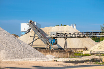 A system of interconnected conveyor belts over heaps of gravel against a blue sky at an industrial cement plant.