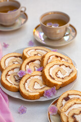 Canvas Print - Tea time. Homemade roll cake with apricot marmalaid and cheese cream and two cups of tea. Decorated with pink flowers. 