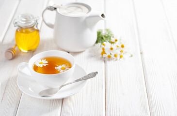 Cup of herbal tea with honey and chamomile flowers on the white wooden background. Natural alternative medicine