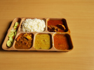 indian chicken thali with rice dal chicken salad vegetable curry on a plastic segmented plate in wooden background