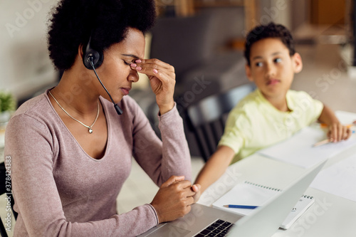 Fotografía African American working mother having a headache while working on laptop at home