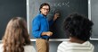 © VAKSMANV - Caucasian man teacher at school writing formulas and mathematics laws on blackboard. School concept. Male lecturer in glasses explaining math laws to pupils. Educational concept.