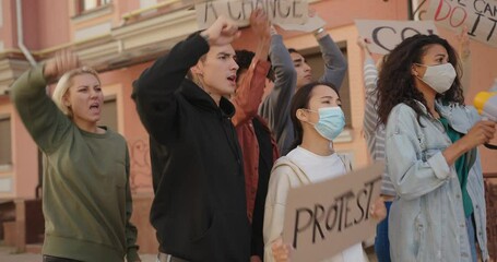 Wall Mural - Mixed race woman in medical mask shouts slogans into megaphone at protest. Multiracial demonstration.