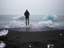 A Tourist Stands On An Iceberg Washed Ashore At Diamond Beach.