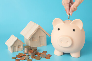 Wall Mural - Model house, coins stack, Pig piggy bank, hand holding a coin on blue background  for money saving concept