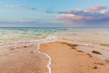 Seashore at sunset, sand is washed from two sides by waves, clouds in the sky