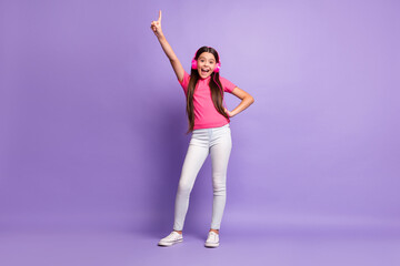 Wall Mural - Full length body size photo of small girl smiling listening to music pointing with finger laughing isolated on purple color background