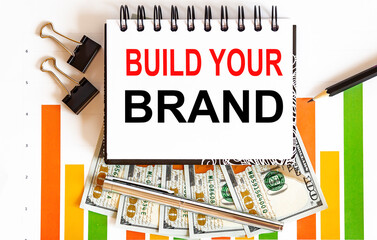 Poster - BUILD YOUR BRAND text on a white background with chart,pencil and dollars