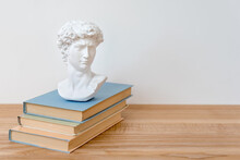 Gypsum Copy Of David's Head On A Bookshelf. Michelangelo's David Plaster Copy Bust Standing On Books. Ancient Greek Sculpture, Statue Of Hero On Wooden Table. Education Concept, Copyspace