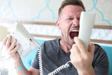 Man Shouts Into White Phone Receiver. Close-up Of Angry Man Rubbing. Guest Hold Phone In His Hand And Talk.