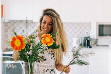 Smiling Young Woman Arranging Flower Bouquet In Kitchen
