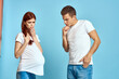 © SHOTPRIME STUDIO - Pregnant woman in white t-shirt and man married couple waiting for baby blue background cropped view of emotions