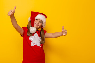 Little girl wearing Santa hat holding thumbs up