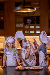 Kid cooking class. Two little girls and teacher chef in kitchen during master class giving high five to eachother