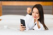 © siraphol - Portrait beautiful young asian woman use smart mobile phone on bed