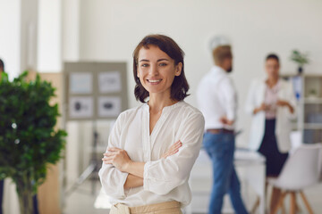 happy successful business lady or company employee standing in office looking at camera and smiling