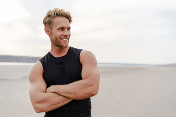 photo of athletic happy sportsman smiling and posing on summer beach