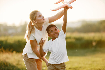 european mother and african son. family in a summer park. people plays with plane.