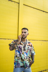 Sticker - Vertical shot of a European male with tattoos calling through his phone against a yellow building