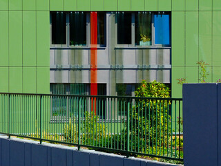 Wall Mural - bright green color glass office building facade detail. decorative windows. steel picket railing and lush green garden in the foreground. modern architecture concept. distinct vertical glass joints