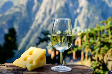 Glass of swiss or savoy dry white wine and yellow emmental cheese with Alpine mountains peaks on background