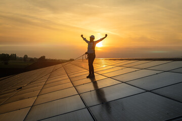 Maintenance assistance technical worker in uniform exulting satisfied with his work after checking operation and efficiency performance of photovoltaic solar panels on roof at sunset.