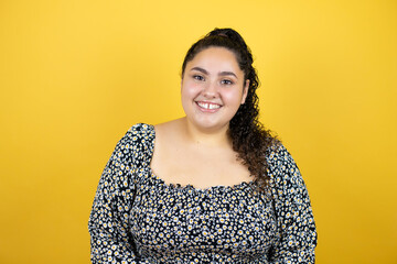 Young beautiful woman with curly hair over isolated yellow background smiling and looking at the camera