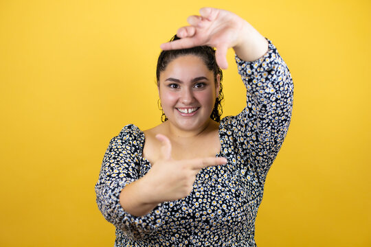Young beautiful woman with curly hair over isolated yellow background smiling making frame with hands and fingers with happy face