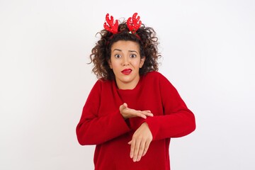 Wall Mural - Young arab woman with curly hair wearing christmas headband standing on white background In hurry pointing to watch time, impatience, upset and angry for deadline delay.