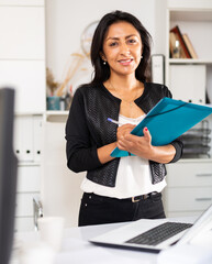 Portrait of successful Hispanic business woman writing down tasks in office ..