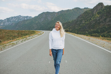 Sticker - Beautiful smiling blonde young woman traveler in white hoodie on road, trip to the mountains, Altai