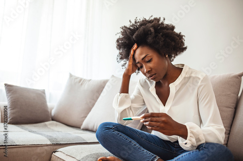 Black woman desperate after reading pregnancy test result. Disappointed african-american girl getting unexpected result from pregnancy test. Shot of a young woman taking a pregnancy test at home