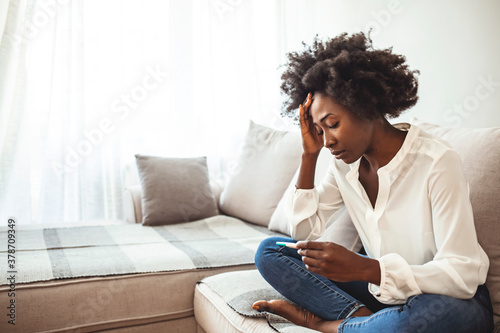 Black woman desperate after reading pregnancy test result. Disappointed african-american girl getting unexpected result from pregnancy test. Shot of a young woman taking a pregnancy test at home