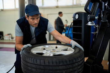 Mid adult mechanic repairing car tire in auto repair shop.