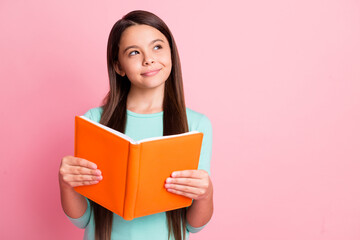 Photo of lovely sweet little ponderous latin lady long hairstyle arms hold orange book sly look up empty space thoughtful wear turquoise teal sweatshirt isolated pink color background