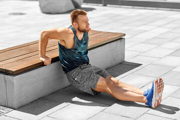 Wall Mural - fitness, sport and training concept - young man doing triceps dip on city street