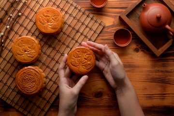 Overhead shot of female hands holding moon cake above table setting in moon festival