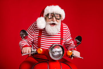 Portrait of his he handsome cheerful cheery bearded Santa father riding moped delivering gifts journey fast speed having fun celebrate isolated bright vivid shine vibrant red color background